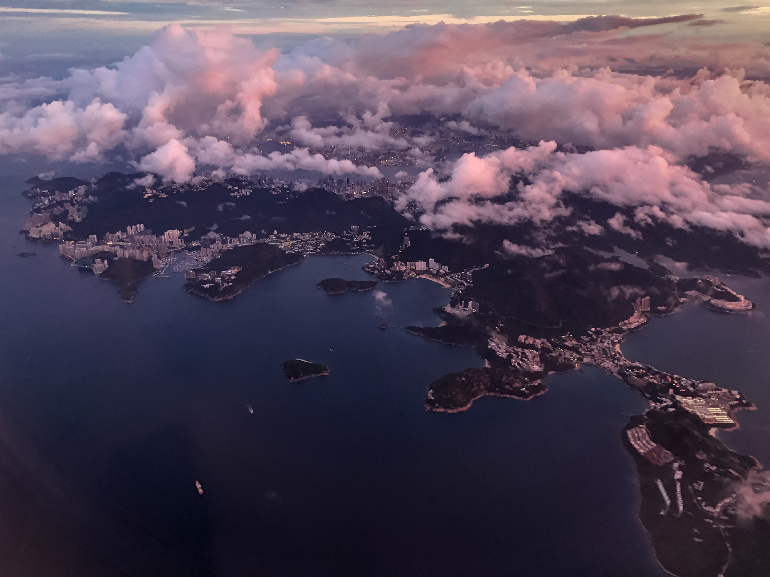 View outside the window of an airplane, showing clouds above the city of Hong Kong at dawn