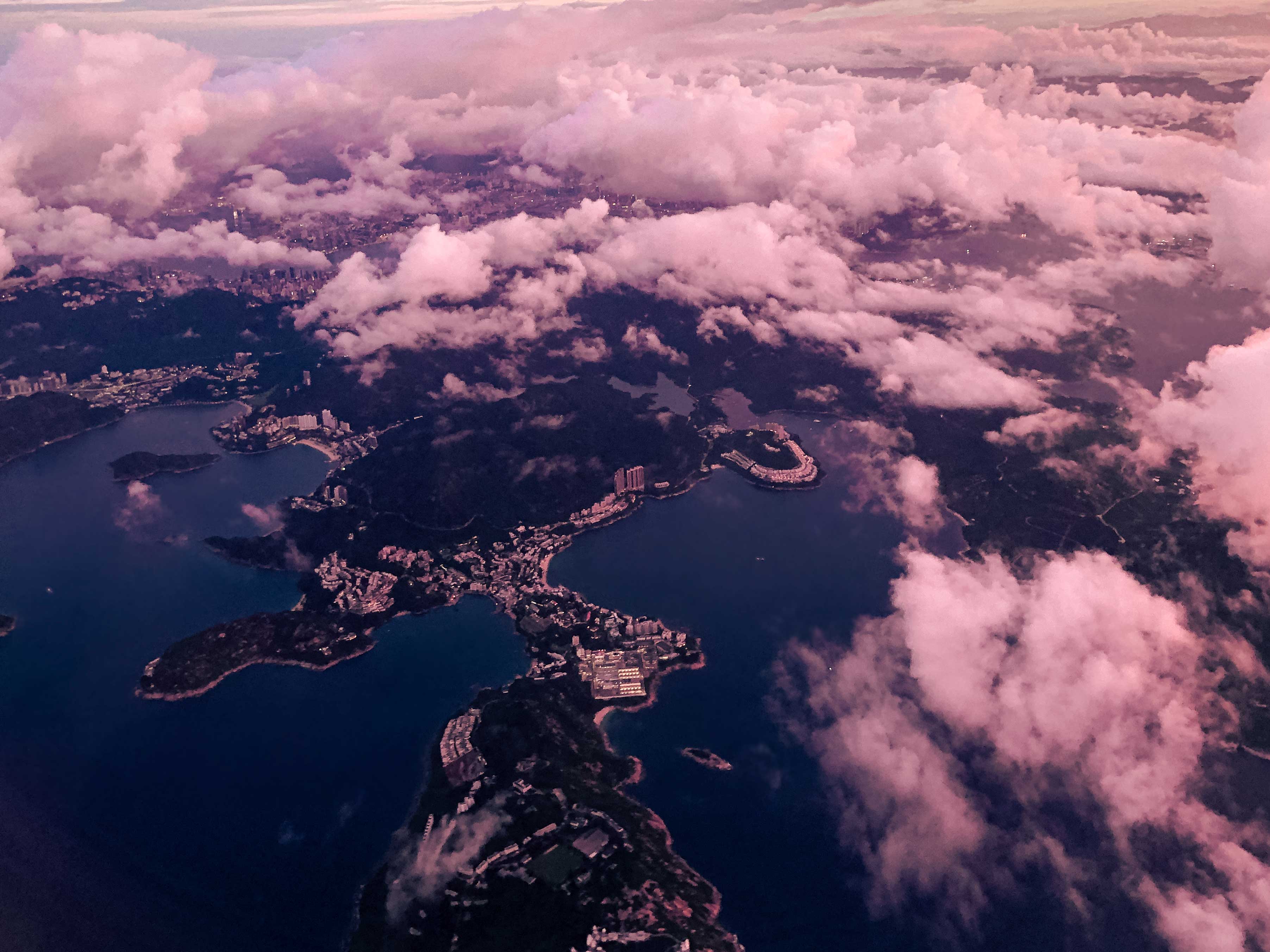 View outside the window of an airplane, showing clouds above the city of Hong Kong at dawn