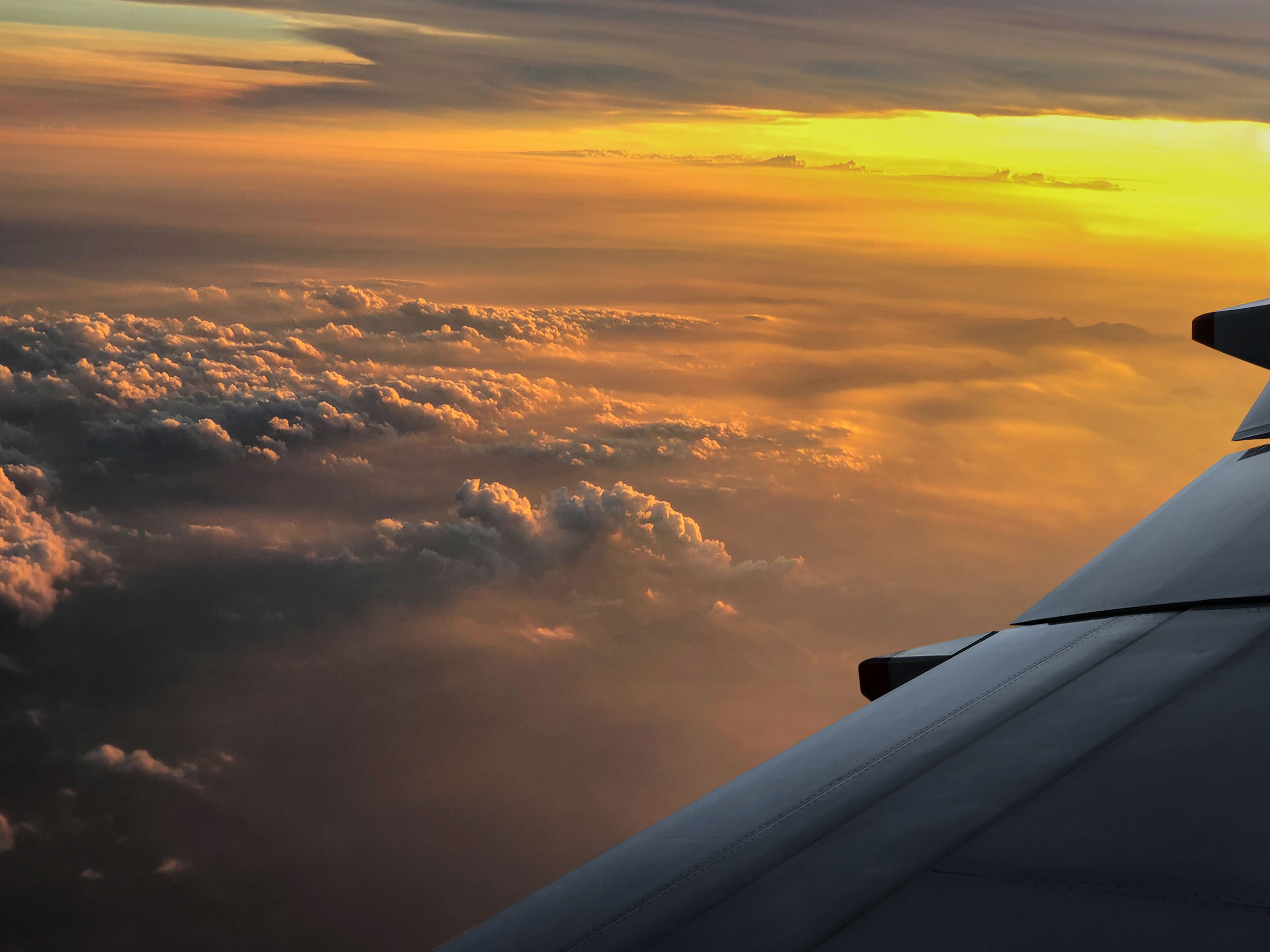 View of the left wing of an airplane, flying above clouds at sunset